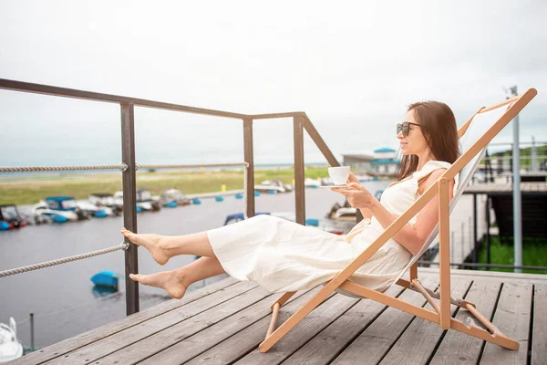 Młoda kobieta pije gorącą kawę ciesząc się widokiem na plażę. — Zdjęcie stockowe