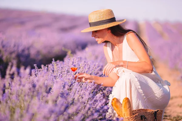 Woman in lavender flowers field at sunset in white dress and hat