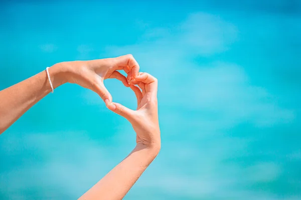 Vrouwelijke handen in de vorm van een hart tegen de turquoise zee — Stockfoto