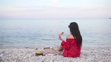 Kadın plajda pizzayla piknik yapıyor.