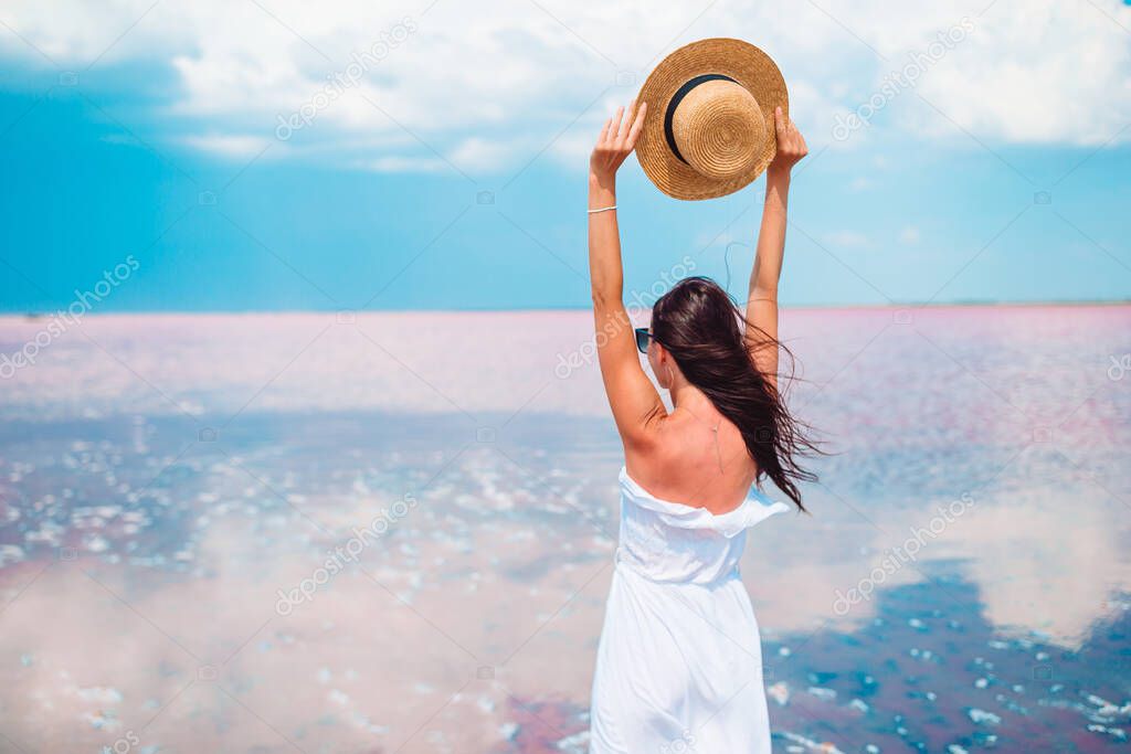 Woman in hat walk on a pink salt lake on a sunny summer day.