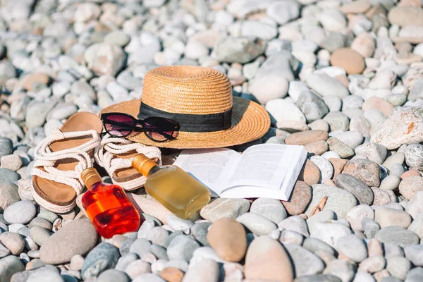 Plaj şapkası açık kitap, güneş kremi ve çakıl taşı plajında ayakkabılar. — Stok fotoğraf
