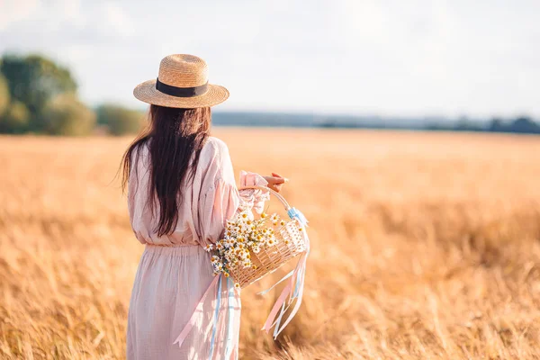 Vista trasera de la niña en el campo de trigo. Hermosa mujer vestida con un sombrero de paja con trigo maduro en las manos — Foto de Stock