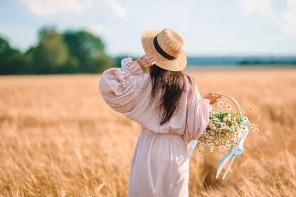 Pohled na dívku v pšeničném poli. Krásná žena v šatech v slamáku se zralou pšenicí v rukách — Stock fotografie