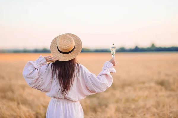 Rückansicht eines Mädchens im Weizenfeld. Schöne Frau im Kleid mit Strohhut und reifem Weizen in den Händen — Stockfoto