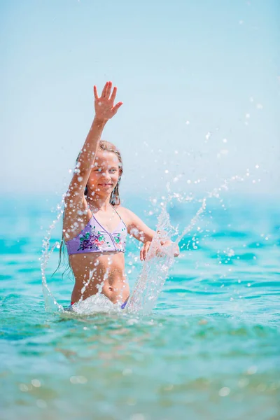 Happy child splashing in the waves during summer vacation on tropical beach. Girl play at the sea. — Stock Photo, Image