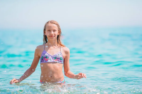 Glückliches Kind, das in den Sommerferien am tropischen Strand in den Wellen planscht. Mädchen spielen am Meer. — Stockfoto