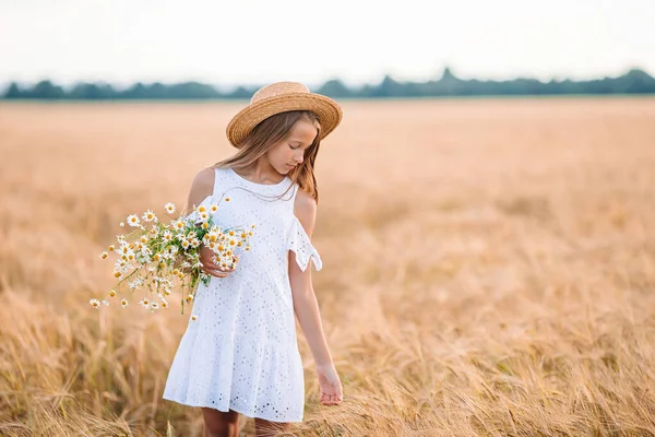 Glückliches Kind im Weizenfeld. Schöne Mädchen in weißem Kleid mit Strohhut und reifem Weizen in den Händen — Stockfoto