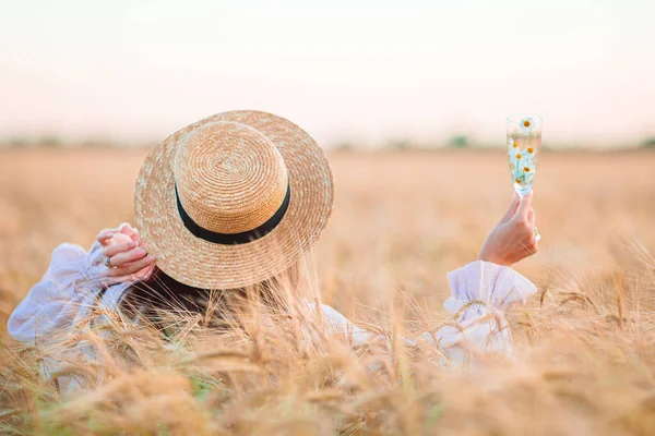 Back view of girl in wheat field. Beautiful woman in dress in a straw hat with ripe wheat in hands — Stock Photo, Image