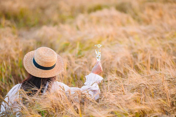 Pohled na dívku v pšeničném poli. Krásná žena v šatech v slamáku se zralou pšenicí v rukách — Stock fotografie