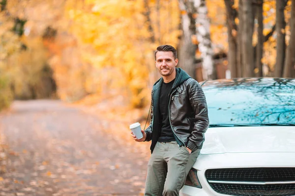 Hombre joven tomando café con teléfono en el parque de otoño al aire libre — Foto de Stock