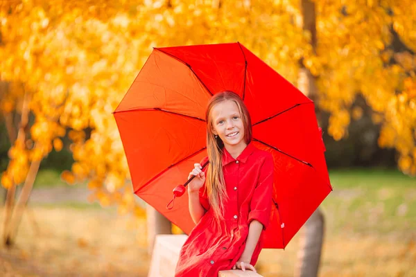 Happy child girl laughs under red umbrella — Stock Photo, Image