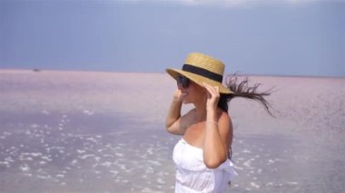 Güneşli bir yaz gününde pembe tuz gölünde yürüyen şapkalı bir kadın..