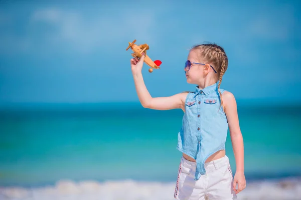 Glückliches kleines Mädchen mit Spielzeugflugzeug in der Hand am weißen Sandstrand. — Stockfoto