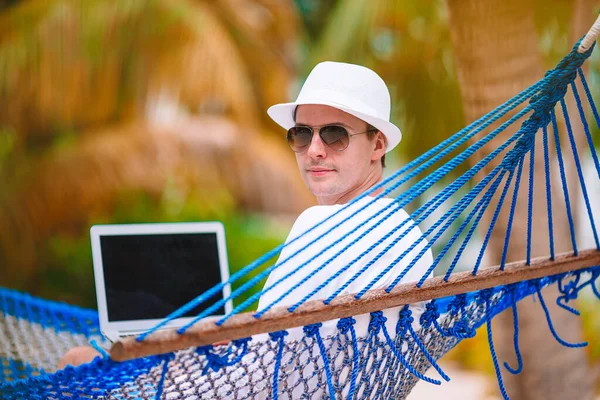 Молодой человек с ноутбуком в гамаке в тропическом отпуске — стоковое фото