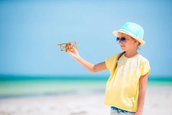 Gelukkig klein meisje met speelgoed vliegtuig in handen op wit zandstrand. — Stockfoto