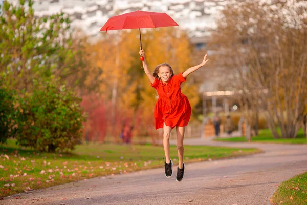 Happy child girl laughs under red umbrella — Stock Photo, Image