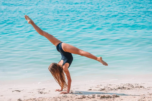 Actief meisje op het strand heeft veel plezier. Schattig kind het maken van sportieve oefeningen op de kust — Stockfoto