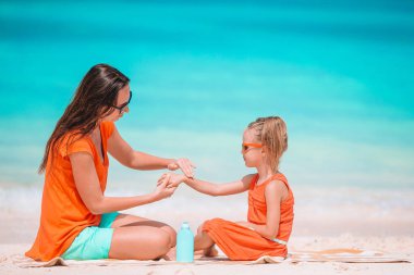 Genç anne sahildeki kızına güneş kremi sürüyor. Güneş koruması