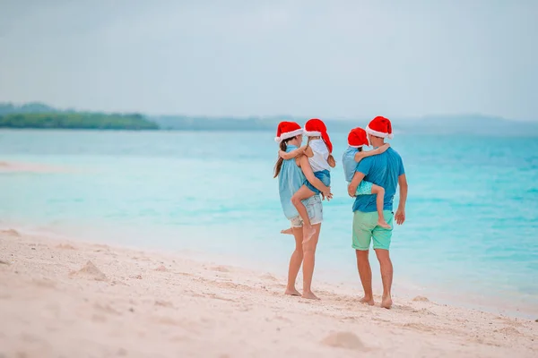 Szczęśliwa rodzina w czerwonych kapeluszach Santa na tropikalnej plaży z okazji świąt Bożego Narodzenia — Zdjęcie stockowe