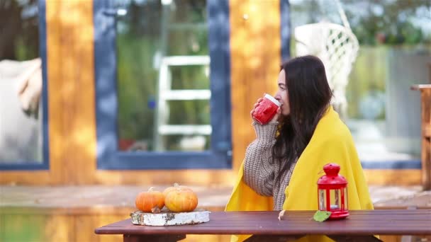Joyeux jeune femme avec téléphone et café assis à la table en bois à l'extérieur — Video
