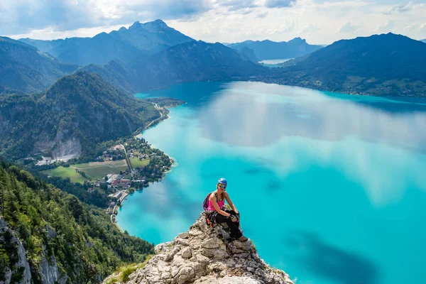 Exhausted but happy girl taking a break on a rock cliff above the turquise waters of Attersee lake, in Upper Austria, during a via ferrata route, on a bright, sunny, summer day.