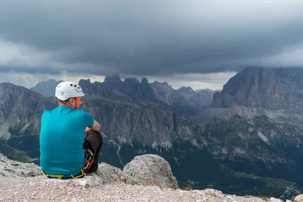 A man pausing after a via ferrata climb on top of Averau mountain peak, in Dolomites, Italy, gazing at the incoming storm