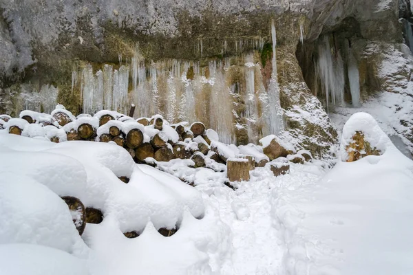 Frozen water columns on a rock wall, with wooden logs cut to size and covered in fresh snow - Winter scene in Seven Ladders Canyon, Piatra Mare mountains (Romania)