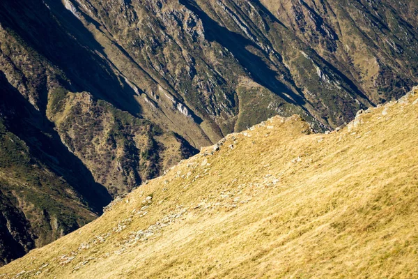 Abstract mountain landscape background with a grass ridge cutting diagonally across rock walls in the back, during a hiking adventure on a sunny day - Fagaras/Carpathian mountains, Romania