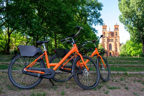 Two orange bicycles parked towards St. Thomas protestant church (Thomaskirche) in Berlin, Germany. Urban bike share concept for weekend gateaways and sightseeing eco friendly city cycle tours.