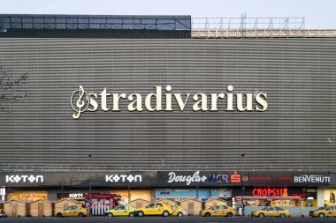 Sarı taksiler Unirea Alışveriş Merkezi Binası önünde park etmiş ve logolar gibi Stradivarius, Koton, Douglas, Bcr, Vodafone kendi cephesinde görüntülenir..