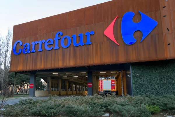 Das Logo des carrefour Supermarktes auf dem Parkett des Einkaufszentrums. carrefour ist eine der größten Supermarktketten der Welt. Feuerwehrauto und Parkausfahrt darunter. — Stockfoto