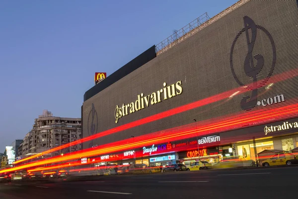 Unirea Shopping Center bâtiment dans le centre de la capitale roumaine, la nuit, avec des taxis jaunes garés devant et des sentiers de lumière de longue exposition photo — Photo