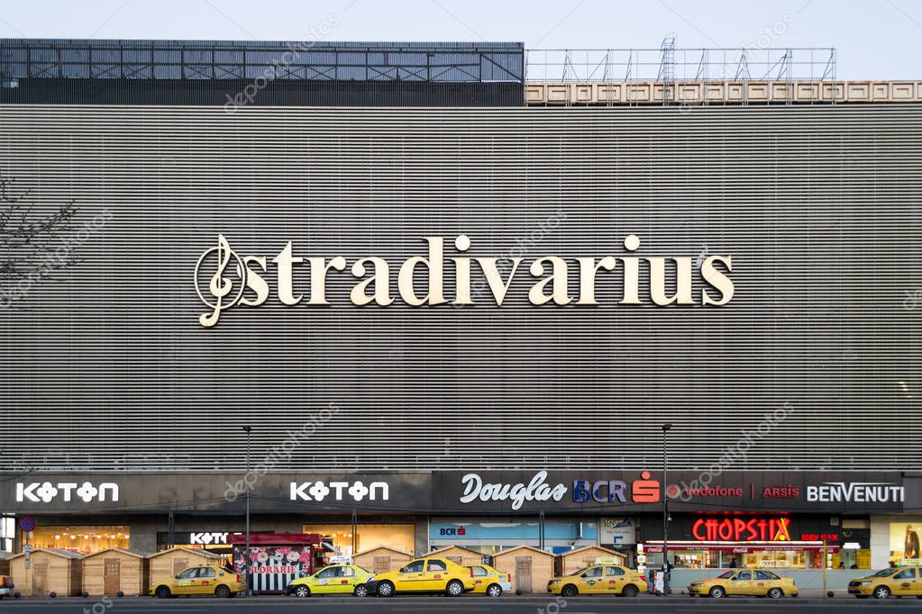 Bucharest, Romania - 17 February 2019:  Unirea Shopping Center building with yellow taxis parked in front and logos such as Stradivarius, Koton, Douglas, BCR, Vodafone displayed on its facade.