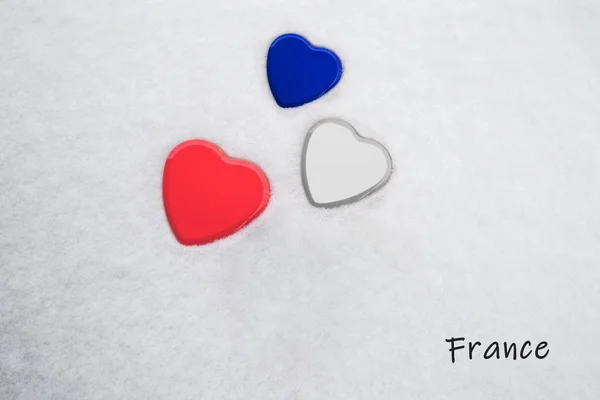 Colori della bandiera francese (blu imperiale, bianco, rosso imperiale) dipinta su tre cuori. Fondo neve con il paese, Francia, scritto in basso a destra. Concetto per una calorosa accoglienza nel turismo . — Foto Stock
