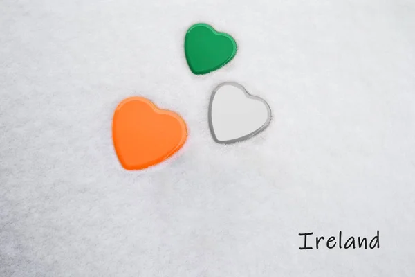 Couleurs du drapeau irlandais (Shamrock Green, White, Mango Tango) peint sur trois cœurs. Fond de neige avec le pays, Irlande, écrit en bas à droite. Concept d'accueil chaleureux dans le tourisme . — Photo