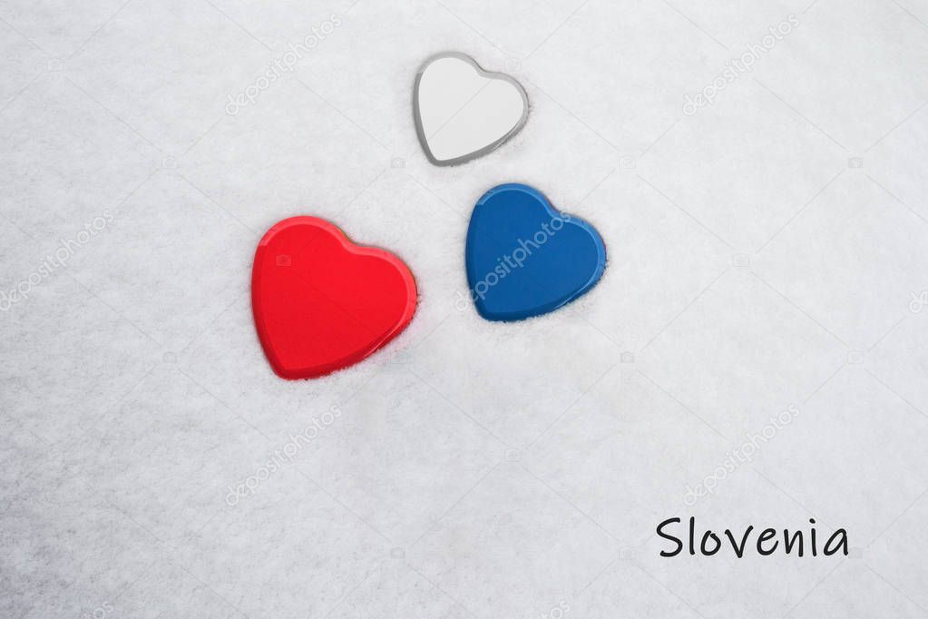 Colors of the slovenian flag (Red (Pigment), Medium Persian Blue, White) painted on three hearts. Snow background with the country, Slovenia, written on bottom right. Concept for tourism.