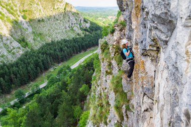 Kadın dağcı karabinalar açılıp bir via ferrata rota, dikey duvar bir yol ile vadi üzerinde. Klettersteig rota Baia de Fier, Pestera Muierilor, Romanya, Gorj İlçesi.