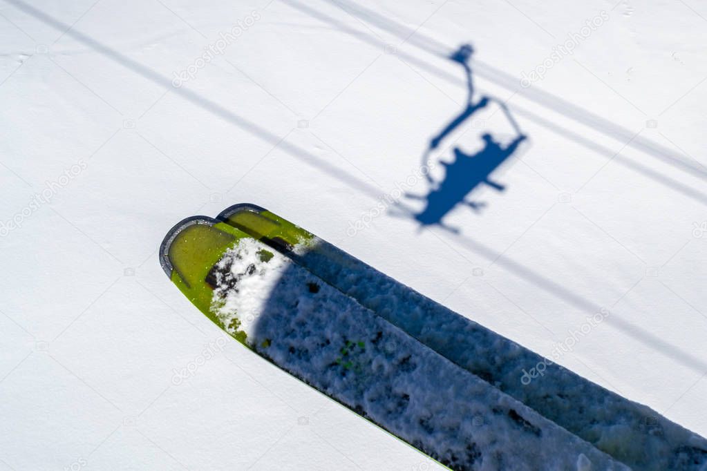 Skis above skiers shadows in chairlift above the white snow, during a Winter ski vacation in Les Sybelles, French Alps. Abstract ski concept with shadows of people in a ski chairlift.