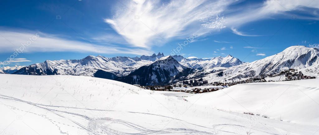 Panoramic landscape with mountain peaks in the French Alps, above La Toussuire village, on a sunny Winter day, in Les Sybelles ski area.
