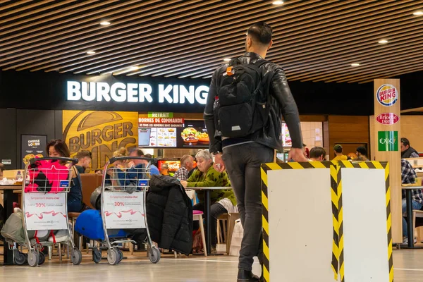 Człowiek, patrząc w kierunku obszaru żywności Burger King w Lyon-Saint Exupery Lotnisko, czekając na jego lot Brama zostanie ogłoszona. Jedzenie na lotnisku - Redakcja. — Zdjęcie stockowe