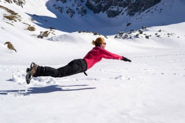 Neşeli kadın yürüyüşçü kar üzerinde atlama, yatay, bir Superman andıran / Superwoman levitating poz, Malaiesti kulübe yakınında, Bucegi / Karpat dağları, Romanya, parlak bir geç Kış gününde.