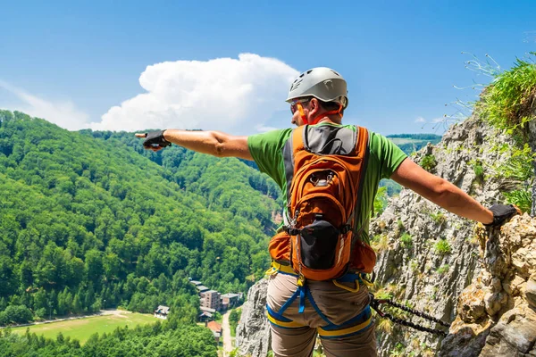 Τουριστικός ορειβάτης που δείχνει το χέρι του σε απόσταση σε μια διαδρομή Via Ferrata στο Baia de Φιέρ, κομητεία Γκόρτζ, Ρουμανία. Αρσενικός ορειβάτης εξοπλισμένος με κράνος, αναρρίχηση, αναρρίχηση σετ και γάντια απενεργοποίησης. — Φωτογραφία Αρχείου