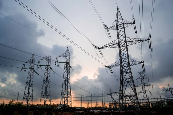 High-voltage electricity grid of power lines, with stormy clouds breaking apart at sunset. Electric transmission towers in a distribution substation in Bucharest, Romania.