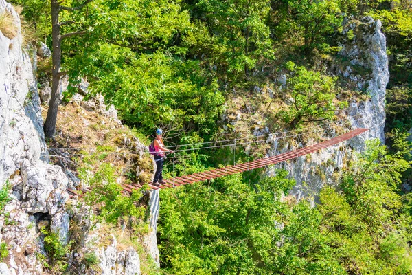 Señora turista en madera suspendida a través de puente de ferrata en una ruta llamada "Casa Zmeului" en Vadu Crisului, Padurea Craiului montañas, Apuseni, Rumania, en un día brillante, caliente, día de verano. Aventura, turismo . —  Fotos de Stock