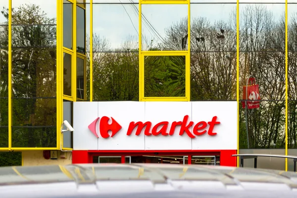 Carrefour-Marktzeichen, rot eingefärbt, über einem Eingang zum Supermarkt, ebenerdig in einem Gebäude mit Glasfenstern. perfekt ausgerichtet auf die Vertikale. — Stockfoto