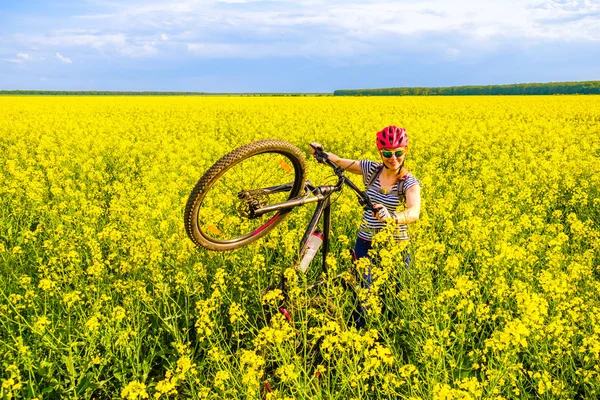 Happy woman with a bicycle in a rapeseed field, during a countryside bike tour in rural parts of Romania, Eastern Europe. Concept for traveling, cycling, eco transportation, photography.