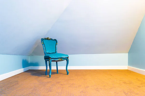 Blue chair isolated in an empty attic room, in a corner, with tungsten light and a brown carpet with spots pattern.