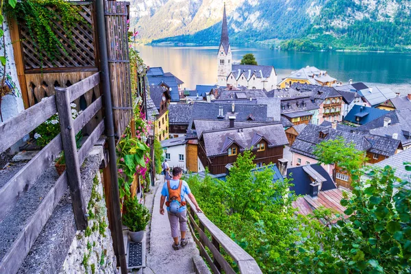 Lidé, kteří chodí dolů po úzkých starých schodech nad Hallstattem, s úchvatným výhledem na jezero Hallstatt (Hallstatter See) a městským kostelem. — Stock fotografie