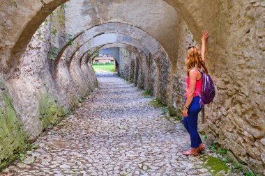Woman tourist looking throw an archway with multiple arches, paved with cobblestone, in Biertan fortified church, Transylvania, Romania, during a sightseeing tour. clipart